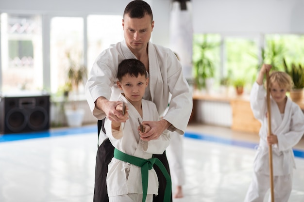 Używanie japońskiej broni. Młoda nauczycielka aikido pomagająca chłopcu w używaniu japońskiej broni podczas ćwiczeń