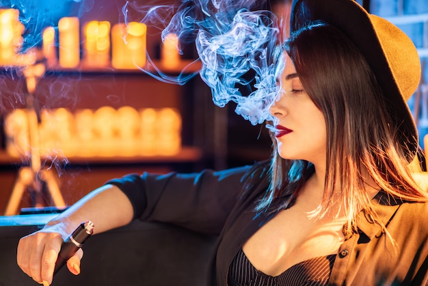 Vaping Młoda piękna dziewczyna dymi elektronicznego papieros w klubie.