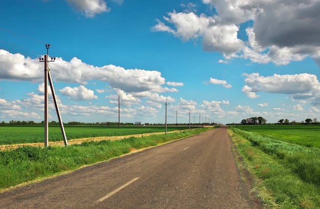 Village Road z linią energetyczną, zielonymi polami i błękitnym niebem z chmurami