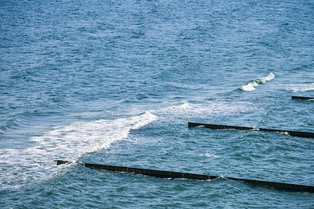 Vintage długie drewniane ostrogi rozciągające się daleko do wód morskich, malowniczy widok na otwarte błękitne morze z pieniącymi się falami. Fale rozbijające się o falochrony. Piękny krajobraz Morza Bałtyckiego, oszałamiający krajobraz morski