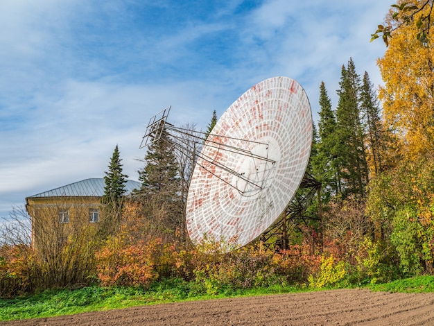 Zdjęcie vintage radio telescope, duża antena satelitarna na tle budynku obserwacyjnego i błękitnego nieba, dawniej radar. koncepcja technologii, poszukiwanie życia pozaziemskiego, podsłuchiwanie przestrzeni.