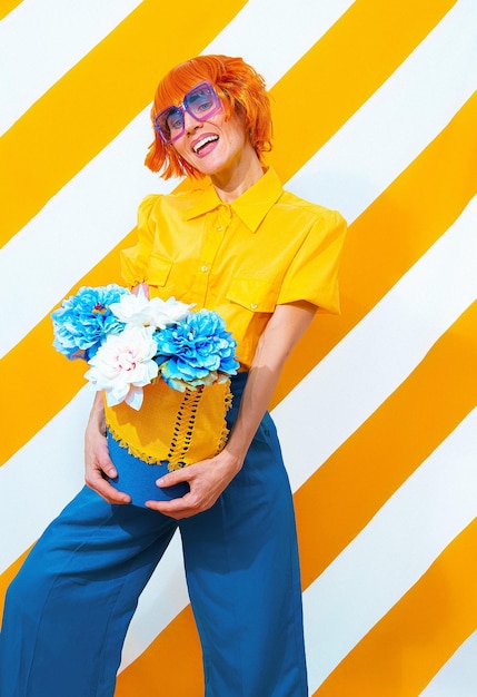 Vintage szczęśliwa dziewczyna na modne paski żółtym tle z układania kwiatów w jej ręce. Minimalna koncepcja wiosna lato