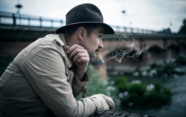 Vintage ubrany mężczyzna palący papierosa w pobliżu starego mostu