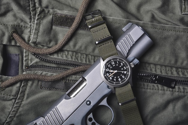 Vintage zegarek wojskowy i pistolet na kurtka wojskowa zielonym tle, klasyczny zegarek mechaniczny zegarek, moda wojskowa męska i akcesoria.