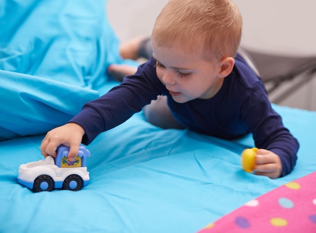 Vrooommmm Mały chłopiec bawi się samochodzikiem na swoim łóżku