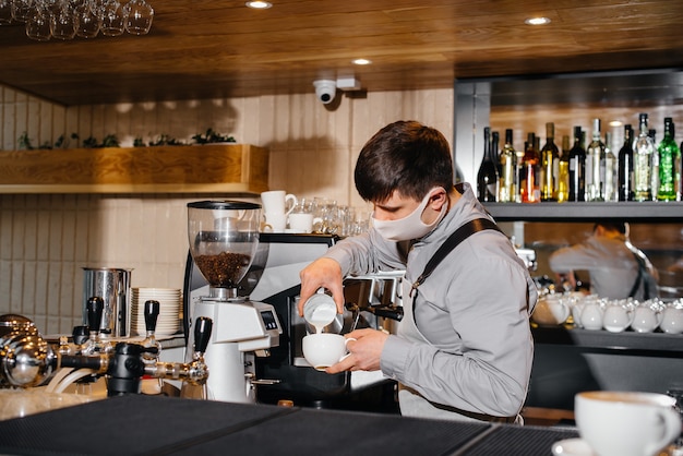 W Barze Kawiarni Zamaskowany Barista Przygotowuje Pyszną Kawę. Praca Restauracji I Kawiarni Podczas Pandemii.