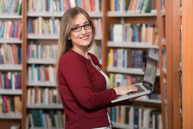 W bibliotece Ładna studentka z laptopem i książkami pracująca w liceum lub bibliotece uniwersyteckiej Mała głębia ostrości