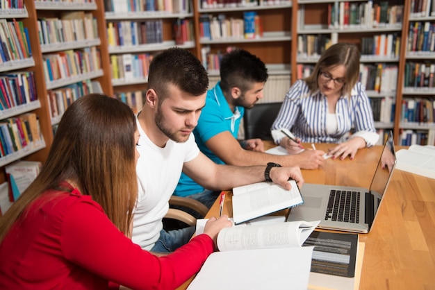 W Bibliotece Przystojna Grupa Uczniów Z Laptopem I Książkami Pracującymi W Bibliotece Uniwersyteckiej Szkoły Średniej Płytkiej głębi ostrości