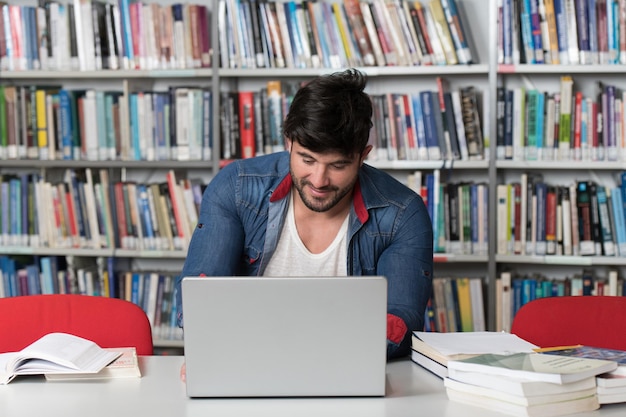 W bibliotece Przystojny student z laptopem i książkami pracujący w bibliotece uniwersyteckiej w liceum Mała głębia ostrości