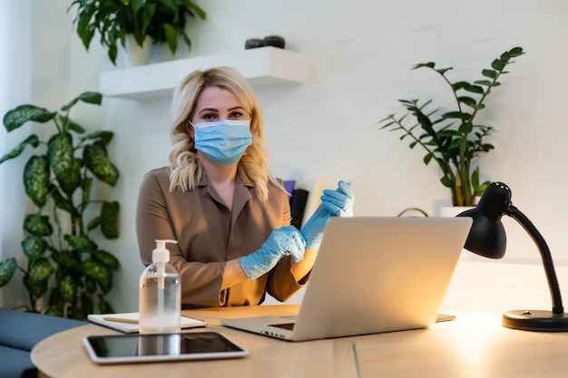 W biurze. kobieta w masce na twarz, dezynfektor stoi obok stołu