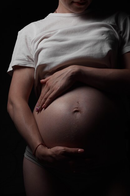 W ciąży piękna młoda kobieta w białej koszulce przytula brzuch z dzieckiem