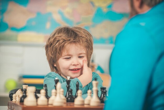 W domu Gry edukacyjne Przedszkolak lub uczeń Wesoły uśmiechnięty chłopczyk siedzący przy stole i okazujący radość podczas gry w szachy