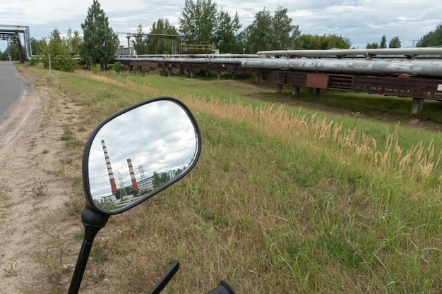 W lustrze motocykla odbija się elektrownia cieplna lub fabryka z dużymi rurami Podróż motocyklem przez teren przemysłowy Zanieczyszczenie powietrza produktami gorenje