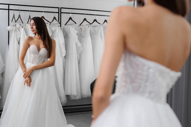 W lustrze odbija się portret panny młodej, która przymierza białą sukienkę ślubną w sklepie.
