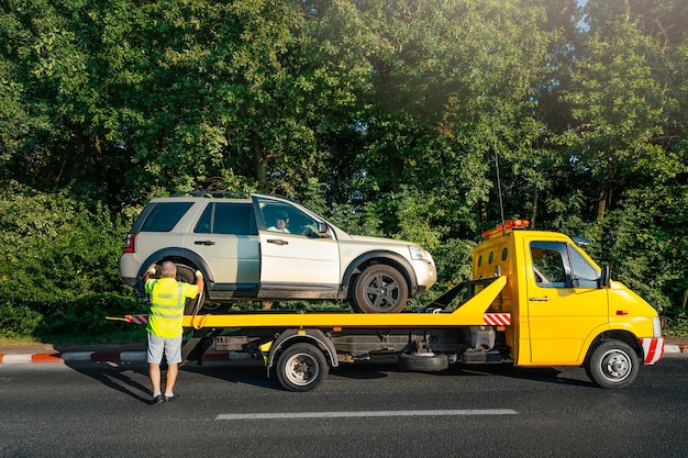 Zdjęcie w mieście ciężarówka holownicza i zepsuty samochód na drodze przeciwko drzewom