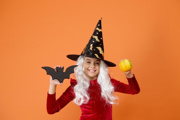 W noc Halloween na pewno będziesz się bać Dziewczyna Halloween w kapeluszu wiedźmy pomarańczowym tle Mała dziewczynka trzyma kij i dynię Halloween Małe dziecko przebrane na imprezę Halloween