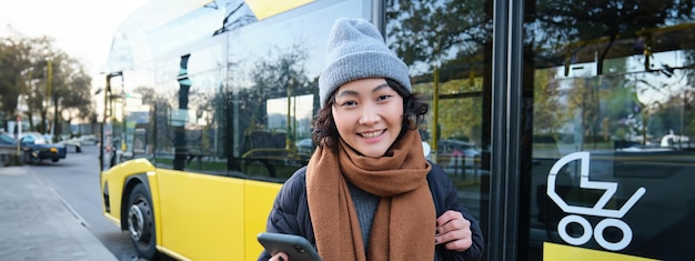 W pobliżu znajduje się zdjęcie studentki oczekującej na rozkład jazdy transportu publicznego w aplikacji na smartfona