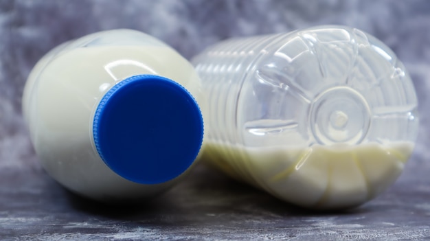 Zdjęcie w połowie pusta i pełna plastikowa butelka świeżego zwykłego mleka leży na ciemnoszarym marmurowym lub betonowym tle. widok z przodu z bliska. koncepcja światowego dnia mleka. płyn odżywczy.