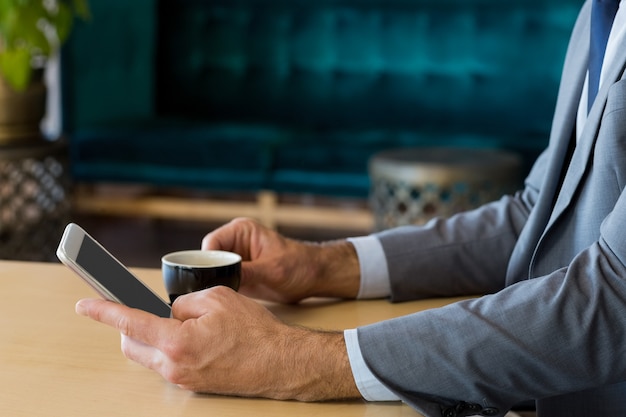 W połowie sekcja biznesmen używa telefon komórkowego podczas gdy mieć filiżankę herbata