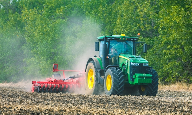 W polu pracuje zielony traktor. Uprawa gleby. Prace rolnicze.