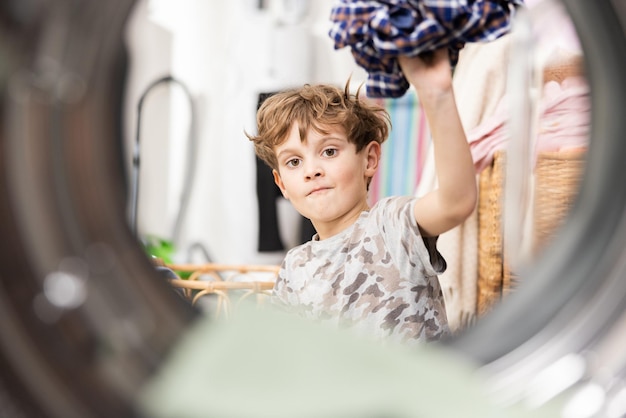 Zdjęcie w pralce mały chłopiec wkłada do bębna kolorowe ubrania