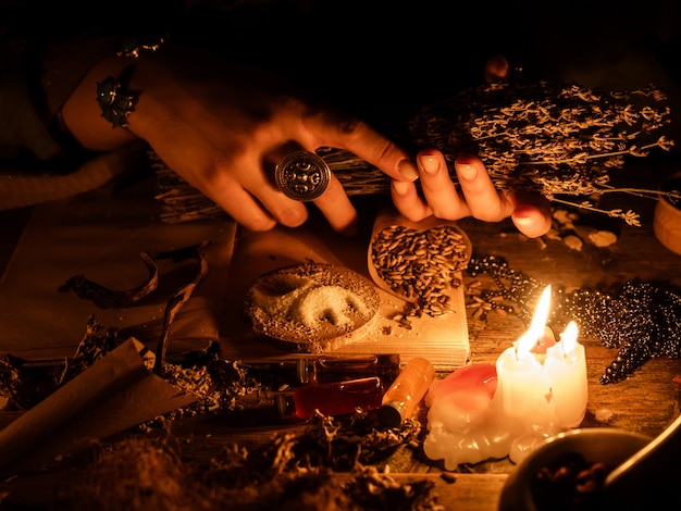W rękach czarownic bukiet suszonych ziół do wróżenia. Światło świec na starym magicznym stole. Atrybuty okultyzmu i magii.