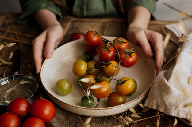 W rękach dzieci talerz z małymi pomidorami na gałęzi.