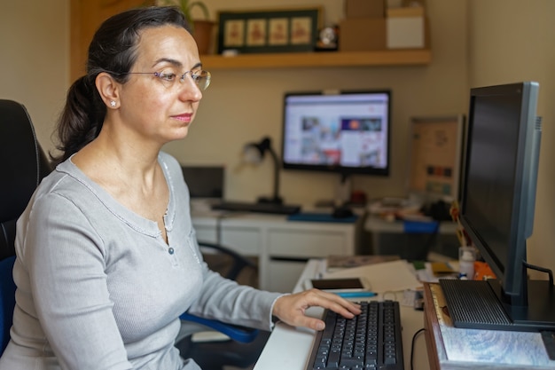 W średnim wieku ładna kobieta z szkłami pracuje w domowym biurze z komputerem