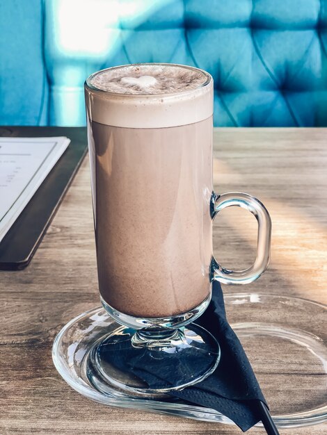 W szklanym kubku kakao napój z sercem z ubitego mleka na stole w restauracji. Fotografia napojów kawowych.