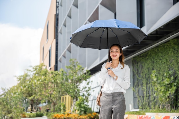 W upalną pogodę młoda bizneswoman trzyma parasol, idąc do biura Jej surowy wyraz twarzy i udane zachowanie są widoczne pomimo gorącej temperatury