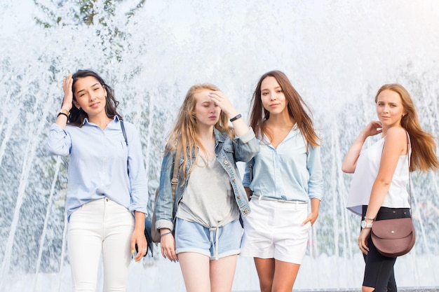 W upalny dzień przy fontannie stoją cztery atrakcyjne kobiety w letnich ubraniach. Grupa atrakcyjnych kobiet.
