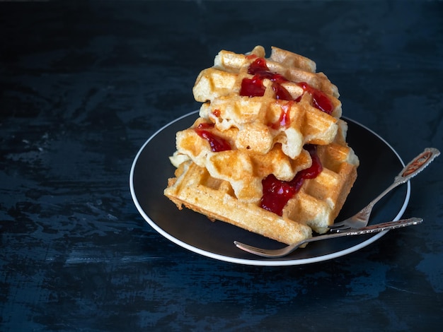 Wafle z serem z dżemem malinowym na ciasnym talerzu z widelcami na deser z bliska