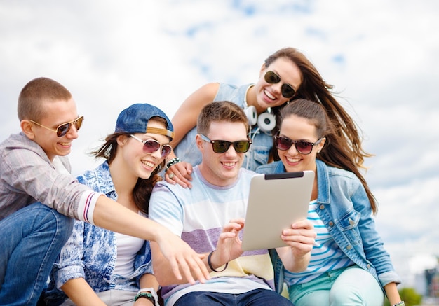 wakacje letnie, koncepcja nastolatków i technologii - grupa uśmiechniętych nastolatków w okularach patrzących na tablet PC na zewnątrz