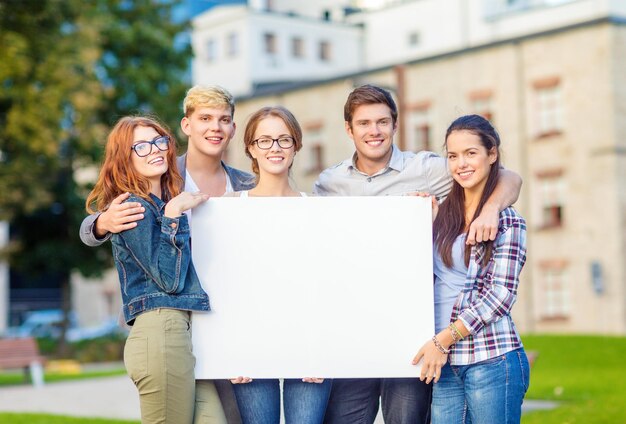 wakacje letnie, reklama, edukacja, kampus i koncepcja młodzieżowa - grupa studentów lub nastolatków z białą czystą tablicą