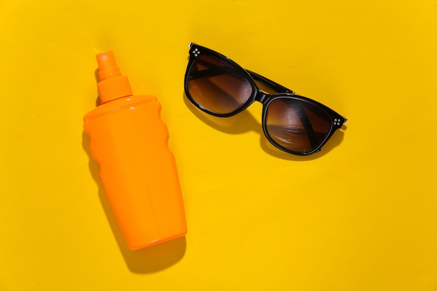 Wakacje na plaży, koncepcja podróży. Butelka z filtrem przeciwsłonecznym i okulary przeciwsłoneczne na żółtym jasnym słonecznym