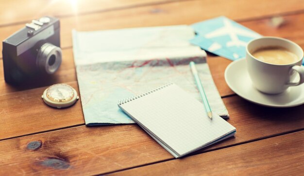 Zdjęcie wakacje, turystyka, podróże i obiekty koncepcja - zbliżenie pustego notatnika z mapą, kawą i biletami lotniczymi