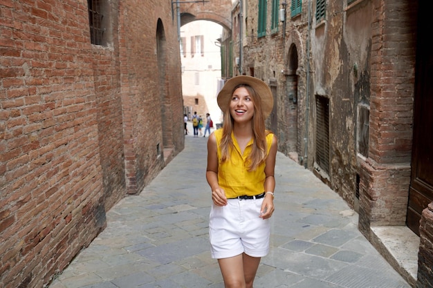 Wakacje w Toskanii Piękna stylowa turystyczna dziewczyna spacerująca między wąskimi uliczkami Sieny zabytkowego miasta Toskania Włochy