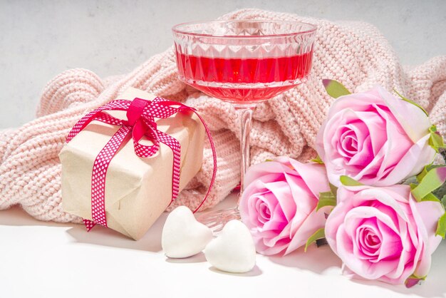 Walentynki, 8 marca, tło kartkę z życzeniami dzień matki. Różowy bukiet kwiatów róży, pudełko rzemieślnicze z czerwoną wstążką, koktajl różany na białym tle stołu