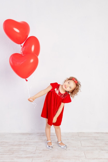 Walentynki dzieci. Mała dziewczynka w czerwonej sukience trzymając balony w kształcie serca