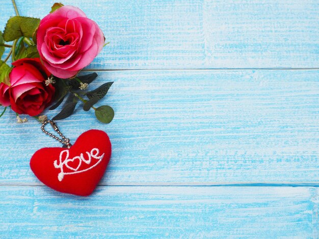 Walentynki kartkę z życzeniami tło z miejsca kopii. Czerwone róże i breloczek czerwony kształt serca ze słowem miłość na niebieskim drewnianym stole.