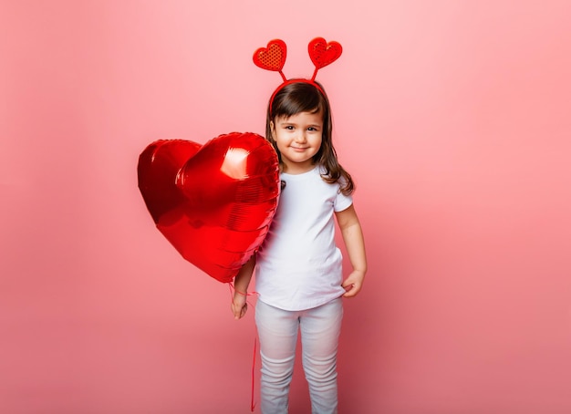 Walentynki, Mała dziewczynka trzyma duży balon w kształcie serca na różowym tle.