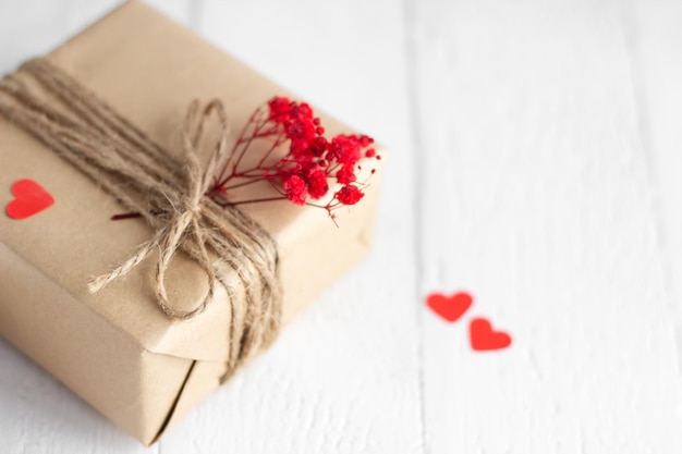 Walentynki pudełko z papieru rzemieślniczego z sercami i czerwonymi kwiatami na białym drewnianym tle