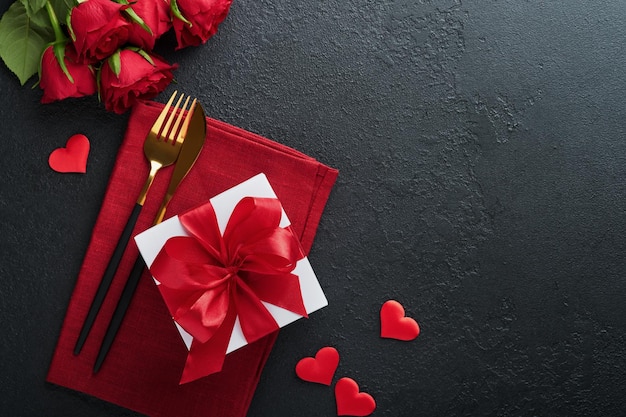 Walentynki romantyczne nakrycie stołu Puste zbliżenie czerwonych róż wino świece obiad czarny talerz nóż widelec i dekoracyjne jedwabne serca na czarnym tle Koncepcja wakacji Kopiuj przestrzeń Widok z góry