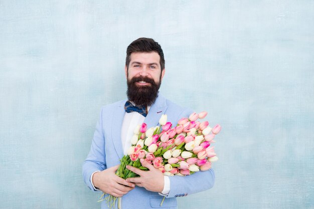 Walentynki są wreszcie tutaj. Brodaty mężczyzna trzyma kwiaty walentynki. Szczęśliwy hipster z bukietem tulipanów. Obchody walentynek. Kwiaciarnie dostarczają na Walentynki. Dzień Kobiet. 8 marca. Wiosna.