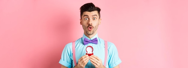 Walentynki zabawny mężczyzna z wąsami i muszką, wyglądający na podekscytowanego i pokazujący pierścionek zaręczynowy