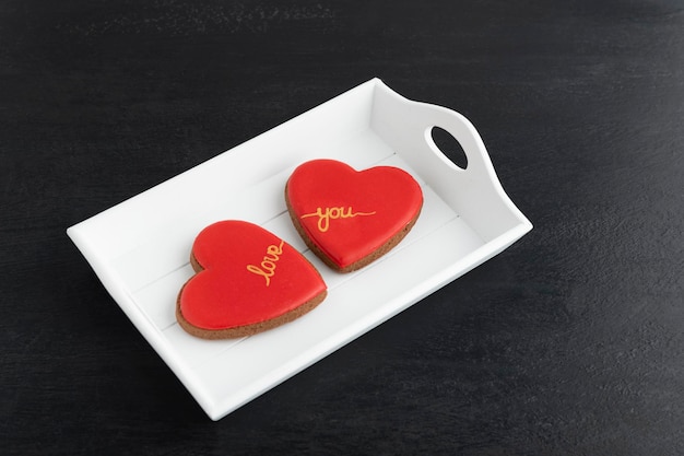 Walentynkowa uczta. Dwa ciasteczka w kształcie serca z czerwonym lukrem na talerzu.