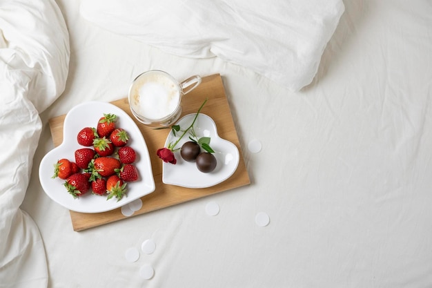 Zdjęcie walentynkowy poranek śniadanie do łóżka truskawkowe cukierki czekoladowe i kawa na drewnianej tacy