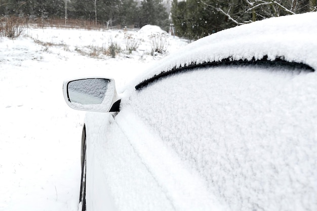 Warstwa śniegu na przedniej szybie lusterka wstecznego samochodu sedan w śniegu w zimie