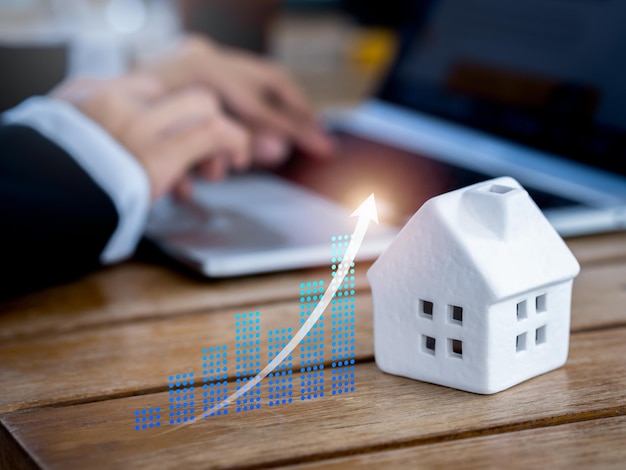 Wartość nieruchomości hipoteka inwestycyjna w nieruchomości i koncepcje podatku od domu Blask wznoszącej się strzałki na cyfrowym wykresie biznesowym w pobliżu białego miniaturowego domu i biznesmena pracującego z laptopem