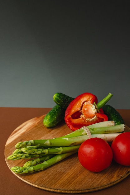 Warzywa leżą na desce pomidory szparagi ogórki czerwona papryka brązowe ciemnoszare tło miejsce na tekst